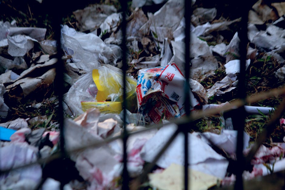 A large pile of black plastic rubbish bags, some tied tightly and others loosely sealed, is stacked against a modern building with a reflective grey and cream tiled facade. The bags appear full and bu